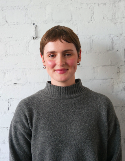 Headshot of Emmerson Lowe, smiling, against a plain white brick wall.